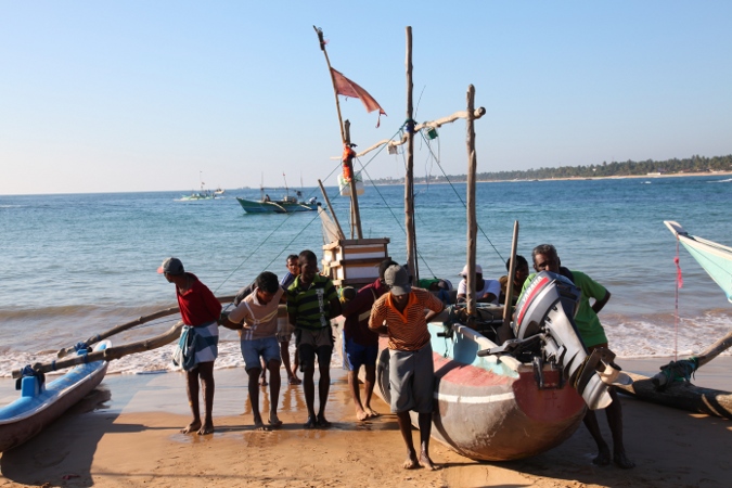 рыбаки спускают лодки на воду в Хиккадуве, Шри Ланка